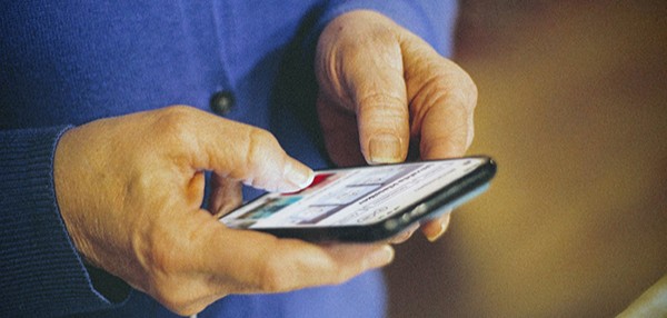 Utsnitt av ein person der ein ser eit par hender som brukar ein mobiltelefon. Foto.